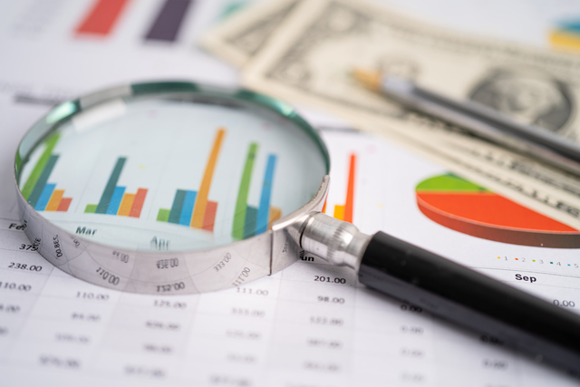 Magnifying glass on charts graphs paper. Financial development, - Kabat, Schertzer, De La Torre, Taraboulos & Co.